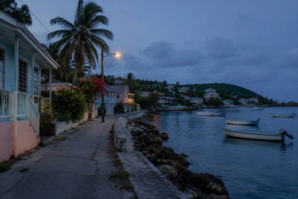 A waterfront street in a small coastal town at twilight with calm water and moored small boats